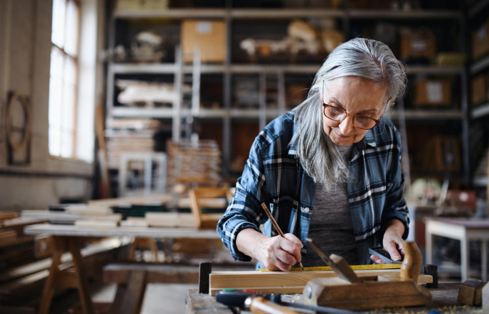 Ältere Handwerkerin, die mit Handwerkzeugen in der Tischlerei arbeitet.