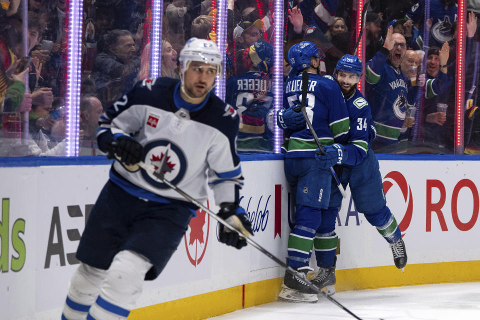 Vancouver Canucks' Teddy Blueger (53) and Phillip Di Giuseppe (34) celebrate Giuseppe's goal, while Winnipeg Jets' Nino Niederreiter (62) skates past during the first period of an NHL hockey game Saturday, March 9, 2024, in Vancouver, British Columbia. (Ethan Cairns/The Canadian Press via AP)