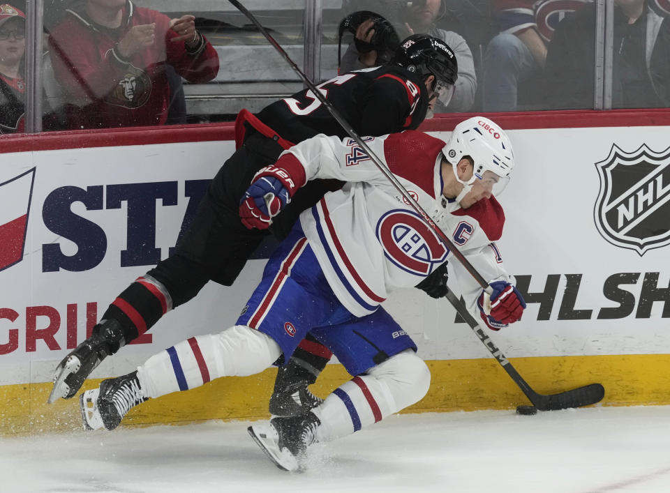 Ottawa Senators defenseman Jake Sanderson, top, battles along the boards with Montreal Canadiens center Nick Suzuki (14) during second-period NHL hockey game action in Ottawa, Ontario, Saturday, April 13, 2024. (Adrian Wyld/The Canadian Press via AP)