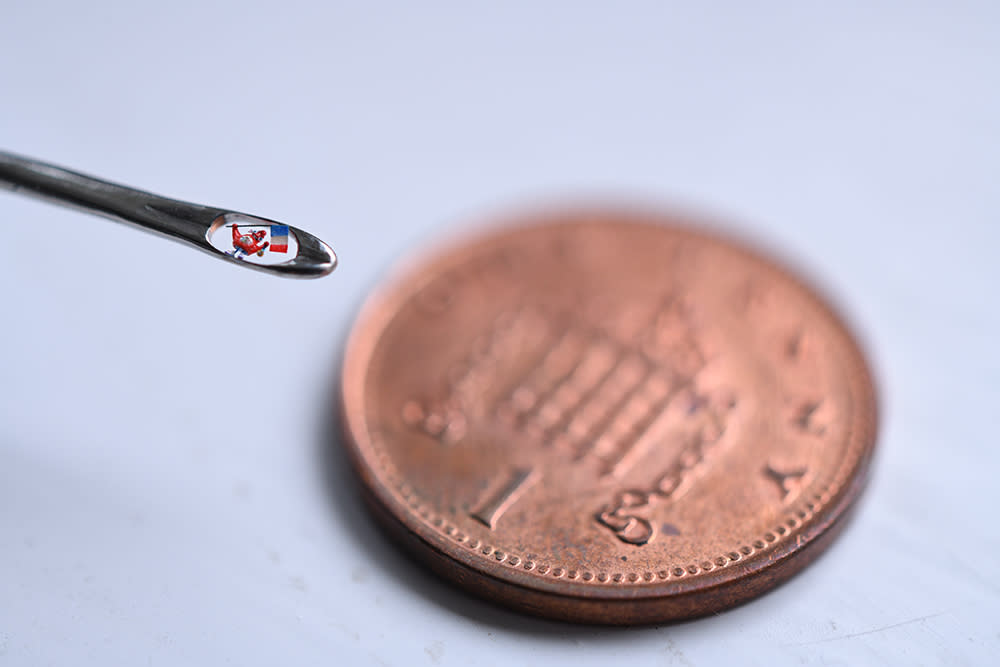 The eye of the needle where the micro-sculpture sits held up alongside a one penny coin 