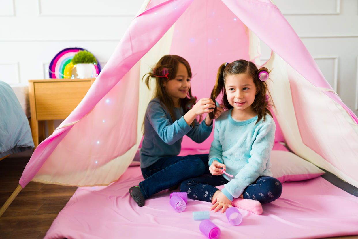 Adorable little girls and best friends playing in a pink teepee doing different hairstyles having fun playdate