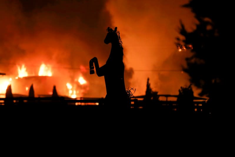 A horse statue is silhouetted by a burning structure during the wind-driven Kincade Fire in Windsor, California