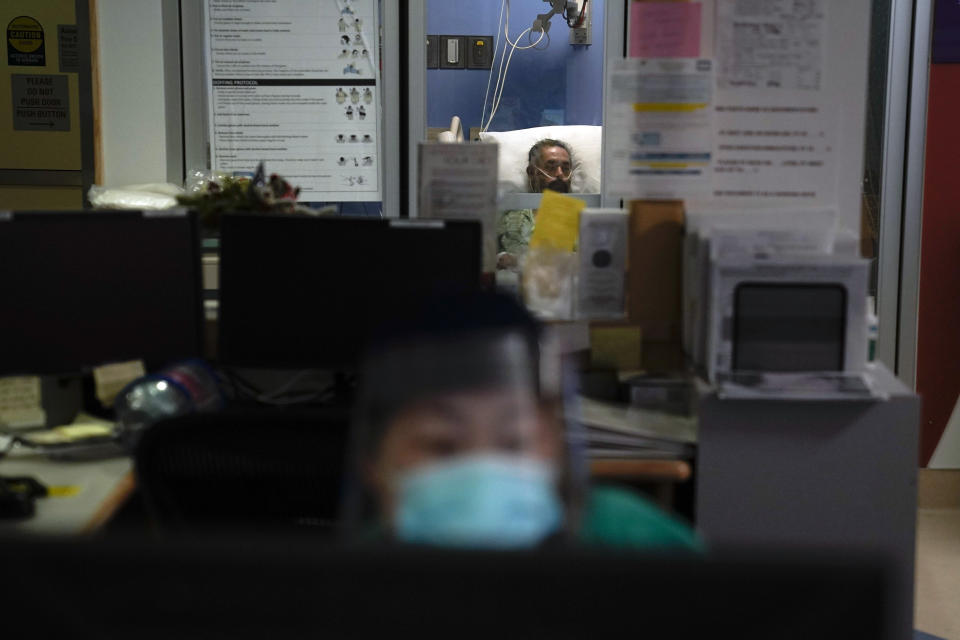 A COVID-19 patient lies in his bed as registered nurse Keran Li, foreground, works on her computer at St. Joseph Hospital in Orange, Calif. Thursday, Jan. 7, 2021. The state's hospitals are trying to prepare for the possibility that they may have to ration care for lack of staff and beds — and hoping they don't have to make that choice as many hospitals strain under unprecedented caseloads. (AP Photo/Jae C. Hong)