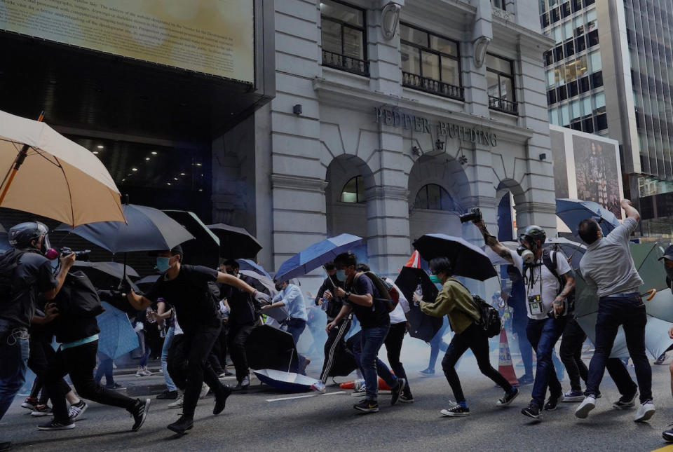 Protesters with umbrellas run after tear gas are fired in Hong Kong on Monday, Nov. 11, 2019. A protester was shot by police Monday in a dramatic scene caught on video as demonstrators blocked train lines and roads during the morning commute. (AP Photo/Vincent Yu)          