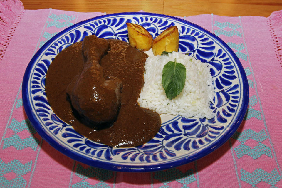 FILE - A plate of chicken in mole sauce served with white rice and fried plantains, prepared by students sits on placemat at the Posada de los Milagros B&B, in Oaxaca, Mexico, March 15, 2011. A hundred years a Dominican nun at the Santa Rosa convent, now a museum, invented the thick brown sauce. It takes days to prepare and contains more than 20 ingredients, from chocolate to peanuts to a variety of chiles deveined to reduce the spiciness. (AP Photo/Luis Alberto Cruz, File)