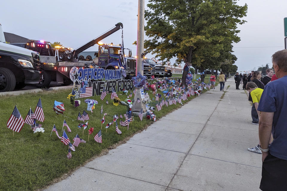 People gather at the memorial site for fallen Fargo Police Officer Jake Wallin on Saturday, July 22, 2023, in Fargo, N.D. Wallin was killed July 14 when a man armed with 1,800 rounds of ammunition, multiple guns and explosives began firing on officers who were responding to a traffic crash.(Ryan Janke/KFGO via AP)