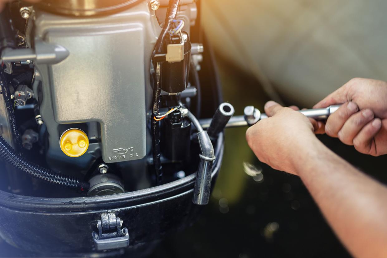 mechanic repairing inflatable motorboat engine at boat garage. Ship engine seasonal service and maintenance. Vessel motor with open cover.