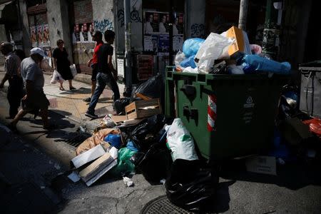 People walk past a pile of garbage in Piraeus, near Athens, Greece June 26, 2017. REUTERS/Alkis Konstantinidis