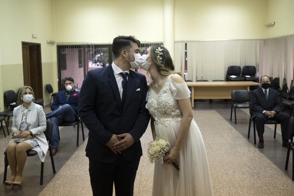 FILE - Groom Raul Benitez and bride Jenny Bonet wear protective face masks as they kiss during their wedding ceremony at the Civil Registry office, in Asuncion, Paraguay, on June 13, 2020. Now that weddings have slowly cranked up under a patchwork of ever-shifting restrictions, horror stories from vendors are rolling in. Many are desperate to work after the coronavirus put an abrupt end to their incomes and feel compelled to put on their masks, grab their cameras and hope for the best. (AP Photo/Jorge Saenz, File)