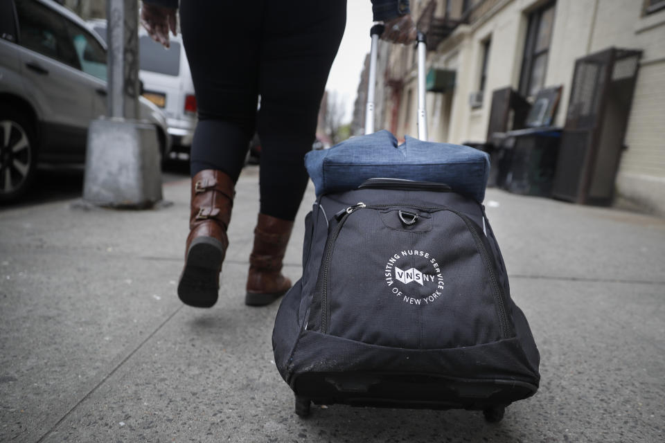 In this Thursday, April 23, 2020 photo, Ruth Caballero, a nurse with The Visiting Nurse Service of New York, pulls her supplies behind her in a rolling case as she makes her rounds in upper Manhattan in New York. Home care nurses, aides and attendants, who normally help an estimated 12 million Americans with everything from bathing to IV medications, are now taking on the difficult and potentially dangerous task of caring for coronavirus patients. (AP Photo/John Minchillo)