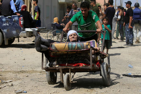 A displaced Iraqi man who fled from clashes, pushes a woman in a cart in western Mosul, Iraq, June 3, 2017. REUTERS/Alaa Al-Marjani