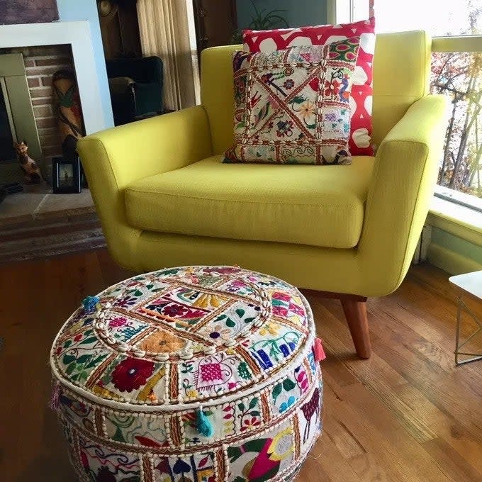 a reviewer photo of the pouf by a yellow chair