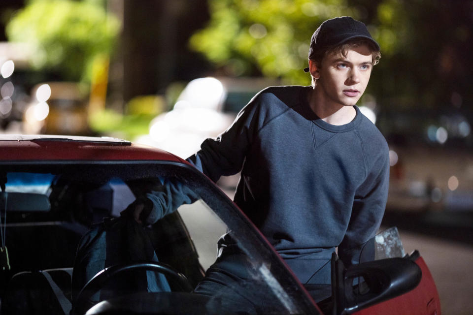 closeup of a teen wearing a baseball cap getting into a car at night