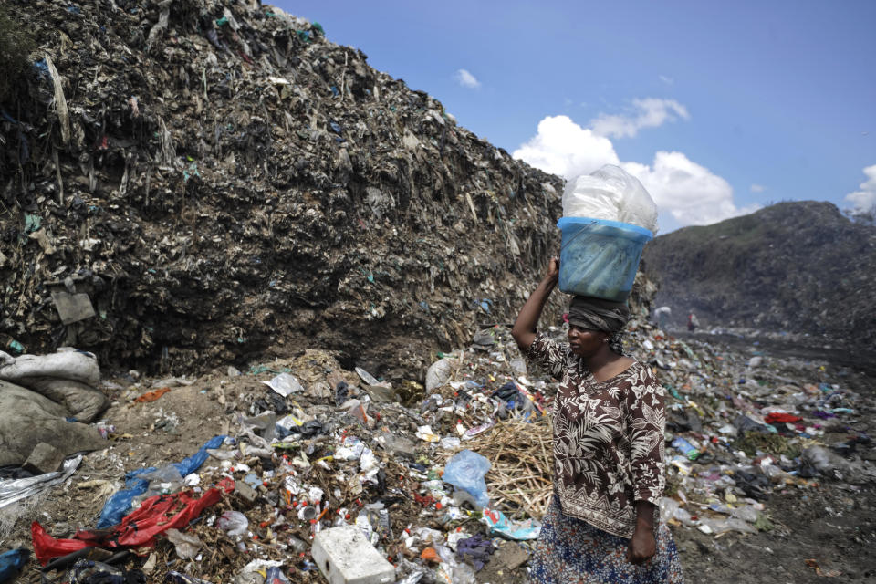 A woman who works selling roasted corn for lunch to people who scavenge garbage for a living walks down a path between hills of garbage at the dump in Dandora, on the outskirts of Nairobi, Kenya, in a December 2018 file photo. / Credit: Ben Curtis/AP
