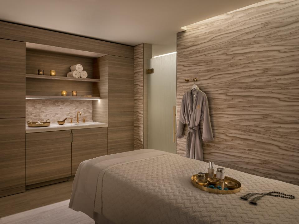 A gray spa treatment room with a bed o the right and a sink behind it to the left