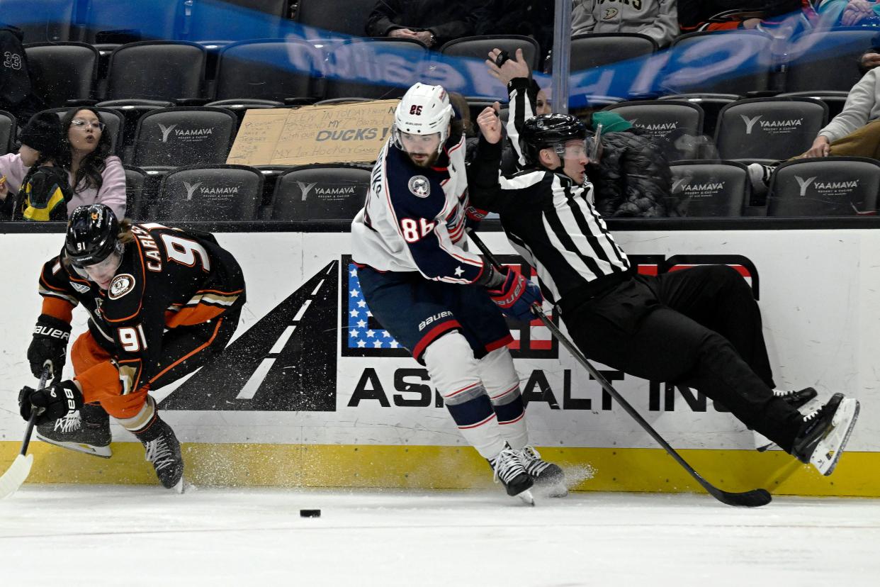 Anaheim Ducks center Leo Carlsson (91) and Columbus Blue Jackets right wing Kirill Marchenko (86) vie for the puck as linesman Mark Shewchyk, right, gets upended during the second period of an NHL hockey game in Anaheim, Calif., Wednesday, Feb. 21, 2024. (AP Photo/Alex Gallardo)
