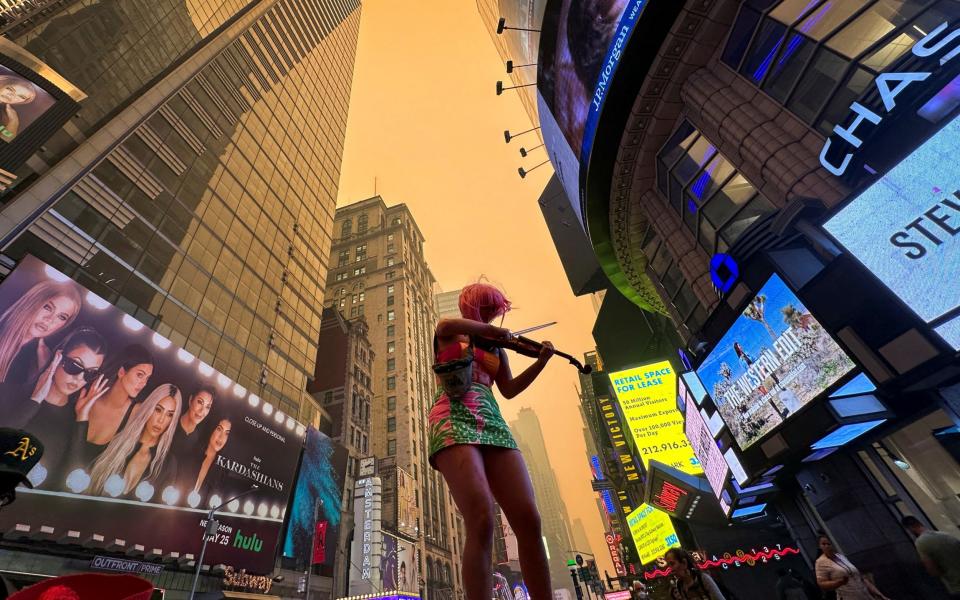 A climate change activist plays a violin in Times Square as Manhattan is shrouded in haze and smoke - MAYE-E WONG/REUTERS