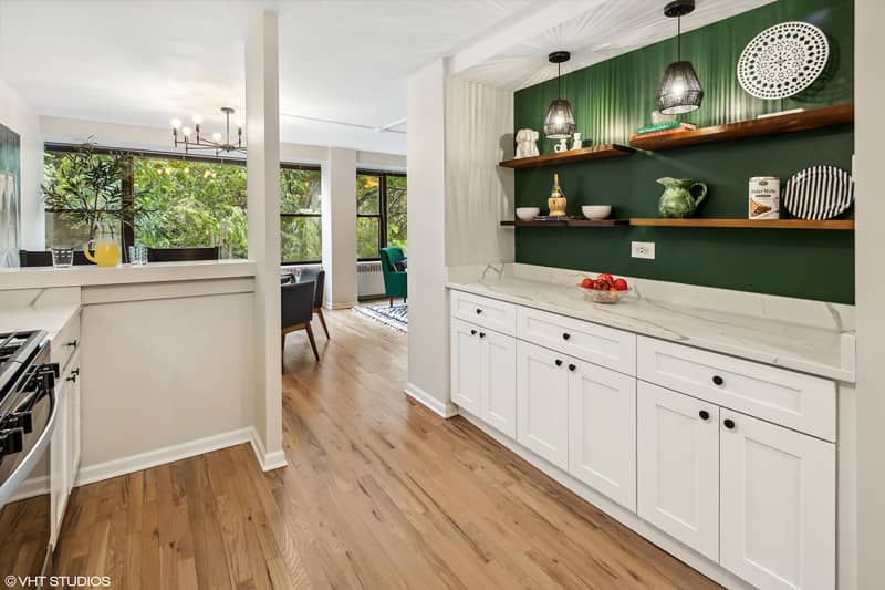 Wooden shelves in front of green painted wall in white kitchen.