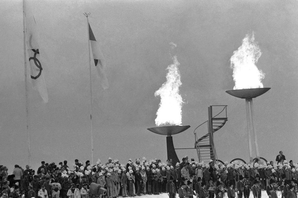 FILE - The Olympic flame of 1976, right and the old one of 1964 Winter Olympics burn in their trays after being ignited in the opening ceremonies for the 12th Olympic Winter Games, on Feb. 4, 1976, Innsbruck, Austria. (AP Photo, File)