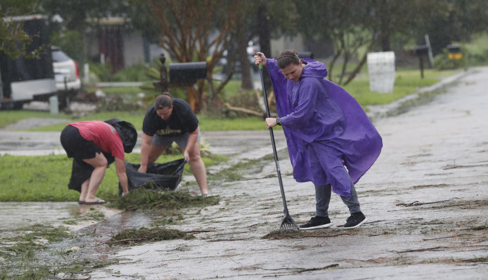 Joni Giandelone, foreground, rakes in the pine needles and branches deposited from Tropical Storm Barry, in front of her house with the help of Priscilla Percle, center, and her mother Gayle Percle in Morgan City, La., Saturday, July 13, 2019. Although they have no trees on their property, a neighbor's tree deposits the pine needles and branches in the street every storm. (AP Photo/Rogelio V. Solis)