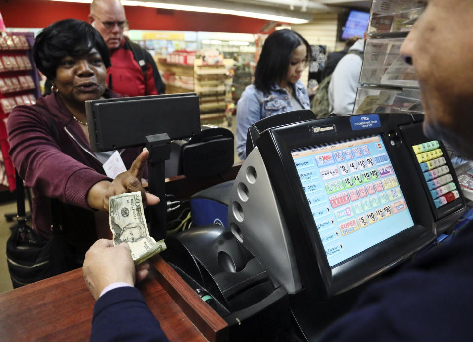 Annette Gray, left, from Valley Stream, N.Y., buys lottery tickets Friday Oct. 19, 2018, in New York. The estimated jackpot for Friday's Mega Millions drawing has soared to $1 billion. Gray said it's about "a dollar and a dream, but I spent ten today". (AP Photo/Bebeto Matthews)