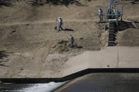 Men in Ciudad Acuna, Mexico, are seen from Del Rio, Texas, as they clean up an area on near a dam along the Rio Grande, where migrants, many from Haiti, had been crossing, Thursday, Sept. 23, 2021, in Del Rio, Texas. The “amistad,” or friendship, that Del Rio, Texas, and Ciudad Acuña, Mexico, celebrate with a festival each year has been important in helping them deal with the challenges from a migrant camp that shut down the border bridge between the two communities for more than a week. Federal officials announced the border crossing would reopen to passenger traffic late Saturday afternoon and to cargo traffic on Monday. (AP Photo/Julio Cortez)