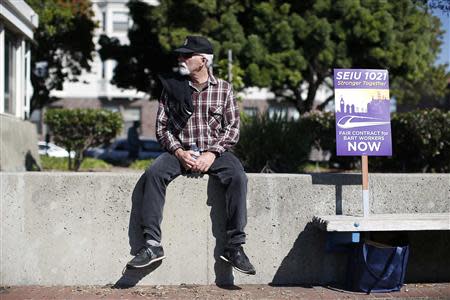 A demonstrator sits next to a sign during a rally in support of striking Bay Area Rapid Transit (BART) workers outside Lake Merritt Station in Oakland