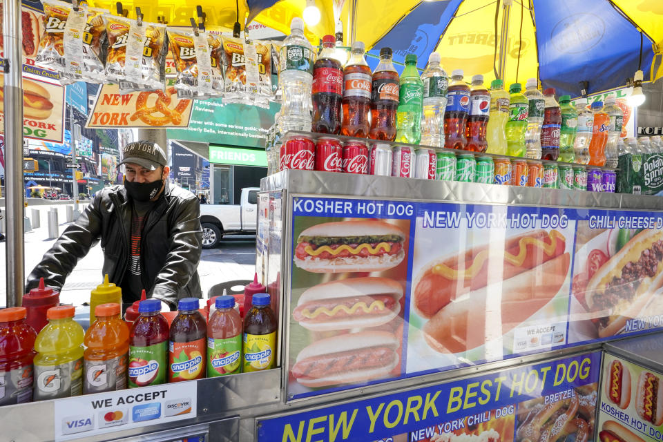 Mohammed Hussein works at his hot dog vending cart in New York's Times Square, Tuesday, April 27, 2021. In recent weeks, tourism indicators for New York City like hotel occupancy and museum attendance that had fallen off a pandemic cliff have ticked up slightly. It's a welcome sight for a city where the industry has been decimated by the impact of the coronavirus. (AP Photo/Mary Altaffer)