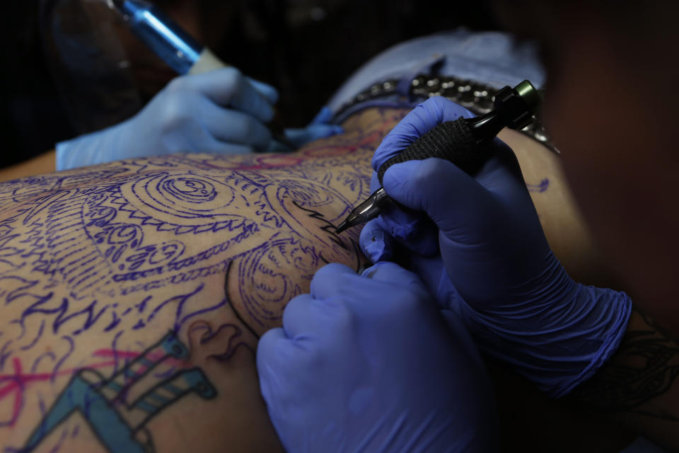 En esta foto del 5 de septiembre de 2018, los tatuadores Lalo Calva y Marco Arana trabajan en un tatuaje que se dibujará en la espalda de Gabriela Irigoyen Aguilar, en el salón de tatuajes Corona en la Ciudad de México. (AP Foto / Marco Ugarte)