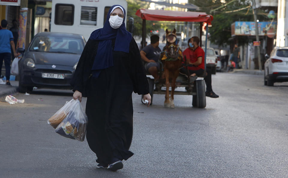 A Palestinian women wears a face mask carries her shopping during a lockdown imposed following the discovery of coronavirus cases in the Gaza Strip, Thursday, Aug. 27, 2020. On Wednesday Gaza's Hamas rulers extended a full lockdown in the Palestinian enclave for three more days as coronavirus cases climbed after the detection this week of the first community transmissions of the virus in the densely populated, blockaded territory. (AP Photo/Hatem Moussa)