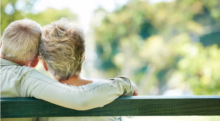 A retired couple relax on a park bench. 