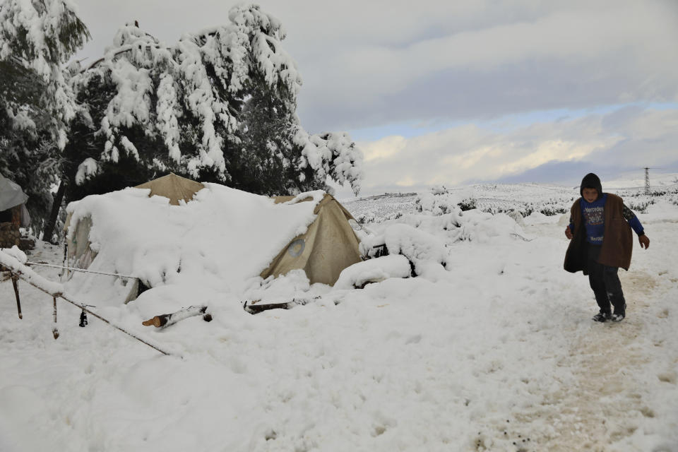 A displaced Syrian boy walk on the snow at a refugee camp, in Afrin, north of Aleppo, Syria, Wednesday, Jan. 19, 2022. A snowstorm in the Middle East has left many Lebanese and Syrians scrambling to find ways to survive. Some are burning old clothes, plastic and other hazardous materials to keep warm as temperatures plummet and poverty soars. (AP Photo/Ghaith Alsayed)