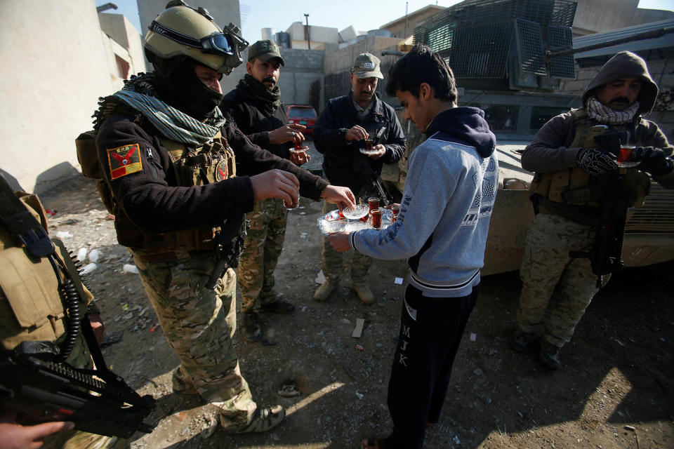 A civilian hands out tea to Iraqi fighters