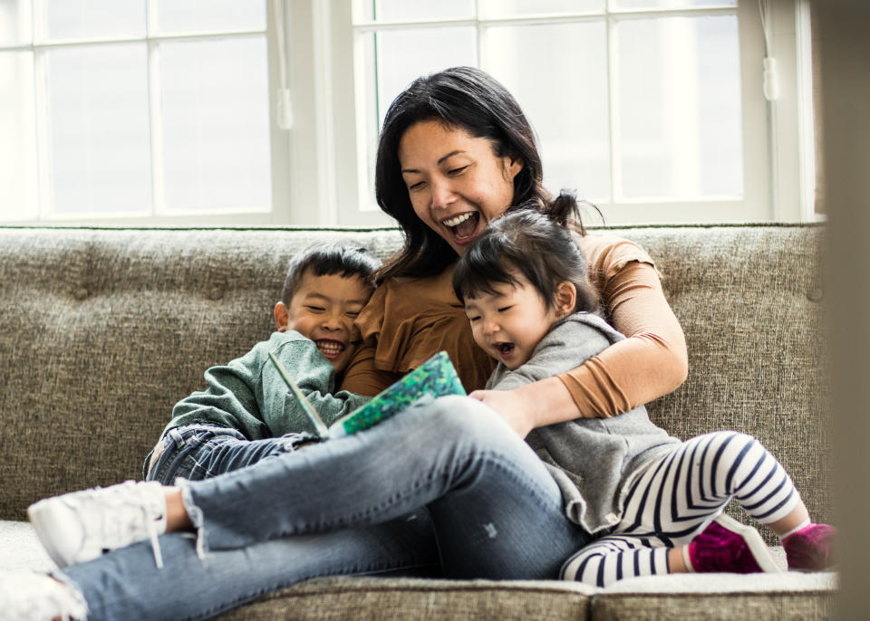 A woman sits on a couch reading a book to two children, all smiling and enjoying the moment