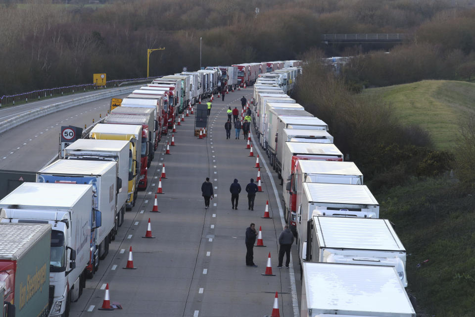 Drivers walk along the road next to freight lorries lined up on the M20 near Ashford, England, Friday Dec. 25, 2020. Thousands wait to resume their journey across The Channel after the borders with France reopened. Trucks inched slowly past checkpoints in Dover and headed across the Channel to Calais on Thursday after France partially reopened its borders following a scare over a rapidly spreading new virus variant. (Gareth Fuller/PA via AP)