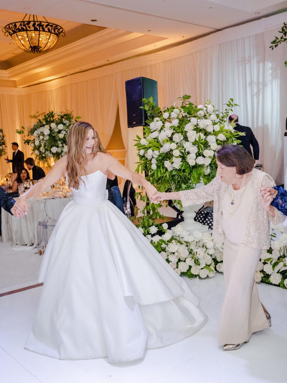 A bride and her grandmother hold hands and dance at her wedding.