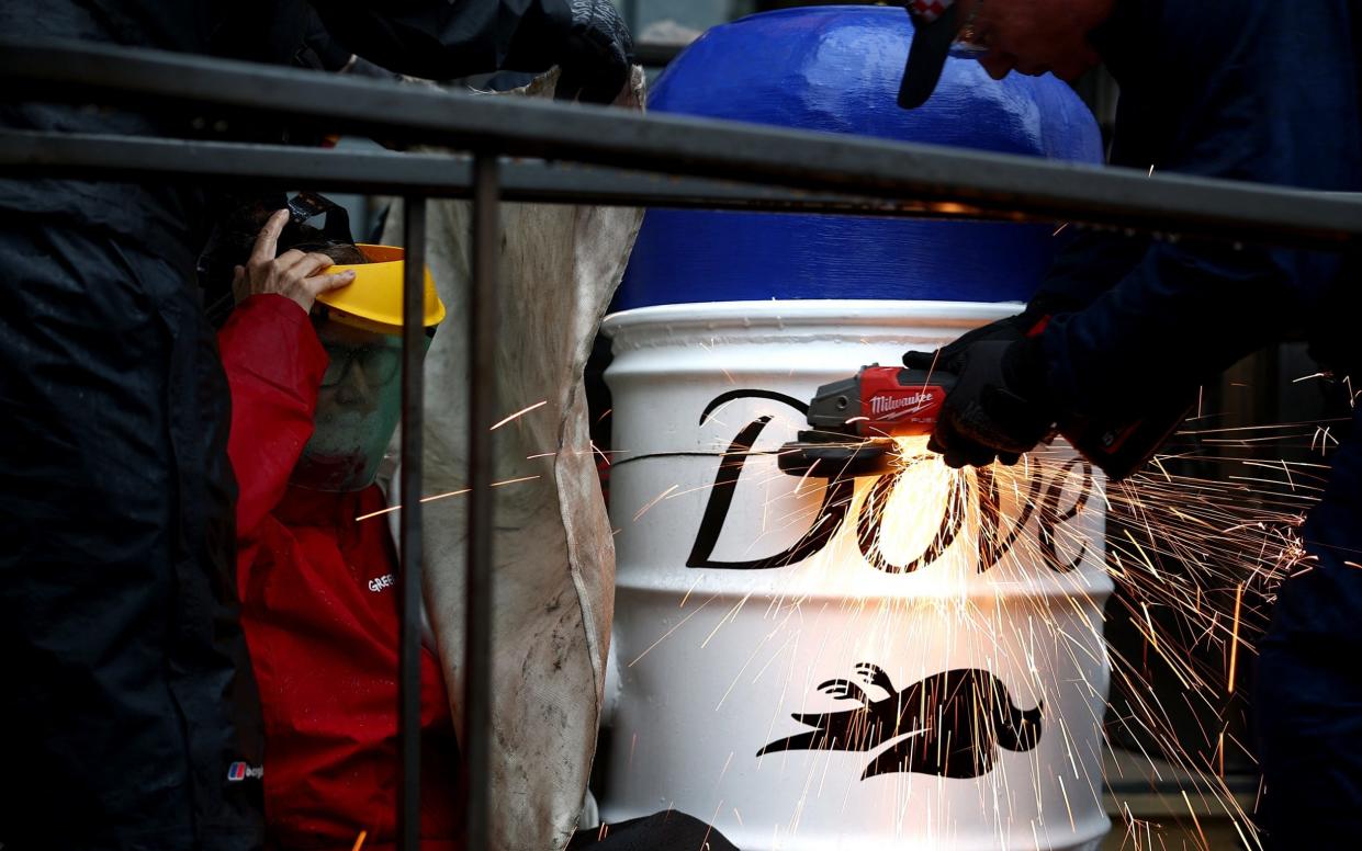 A police officer uses an angle grinder to cut through a mock bottle of deodorant as a Greenpeace activist holds their arm inside the painted barrel outside Unilever's headquarters in London