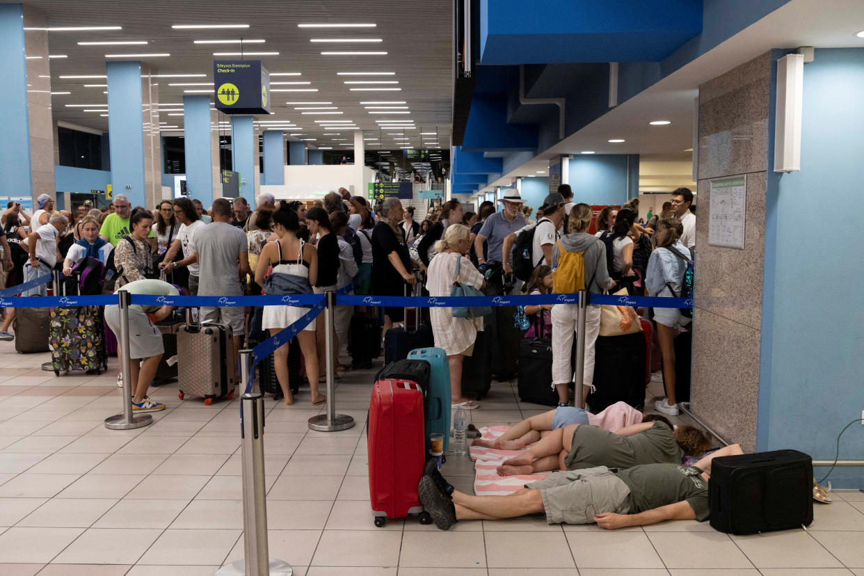 Tourists sleep as others line up at check-in counters, while waiting for departing planes at the airport, after being evacuated following a wildfire on the island of Rhodes, Greece, July 24, 2023. REUTERS/Nicolas Economou