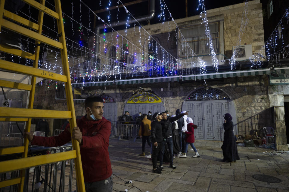 A Palestinian man holds a ladder for another man stringing colored lights on the eve of the Muslim holy month of Ramadan in the Old City of Jerusalem, Monday, April 12, 2021. (AP Photo/Maya Alleruzzo)