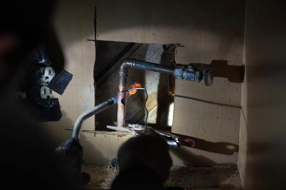 CORRECTS SPELLING OF LAST NAME TO VALERIO, NOT VALERIA - Handyman Roberto Valerio works on repairing a broken pipe beneath the sink in the home of Nora Espinoza, on Saturday, Feb. 20, 2021, in Dallas. The pipe broke during freezing temperatures brought by last week's winter weather. (AP Photo/Tony Gutierrez)