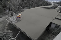 In this Jan. 14, 2020, photo, a resident clears volcanic ash from his roof in Laurel, Batangas province, southern Philippines. Taal volcano is spewing ash half a mile high and trembling with earthquakes constantly as thousands of people flee villages darkened and blanketed by heavy ash. (AP Photo/Aaron Favila, File)