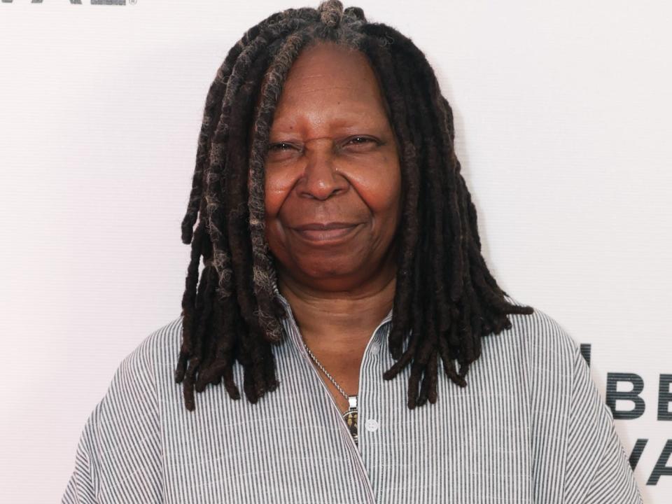 Whoopi Goldberg poses for photos in a striped shirt dress.