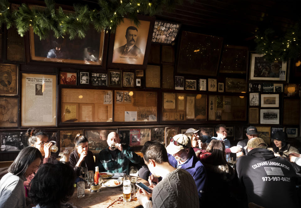In this Dec. 27, 2019 photo, customers sit beneath vintage photos and documents, including a poster of Vice President Theodore Roosevelt, in McSorley's Old Ale House in New York. Located in Manhattan's Lower East Side, McSorley's opened in the mid-19th century and functioned as a speakeasy during Prohibition. (AP Photo/Mark Lennihan)