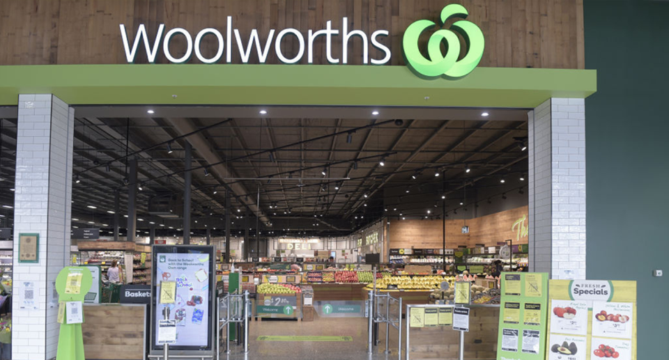 A Woolworths store front with promotional signs at the entrance and the large logo overhead. 