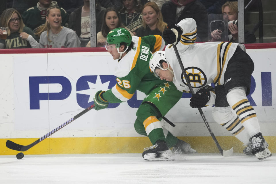 Minnesota Wild center Connor Dewar (26) controls the puck as Boston Bruins defenseman Ian Mitchell challenges during the first period of an NHL hockey game Saturday, Dec. 23, 2023, in St. Paul, Minn. (AP Photo/Abbie Parr)