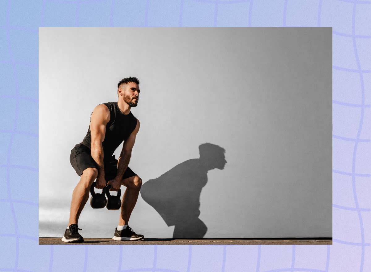 muscular man lifting two kettlebells outdoors in front of cement wall