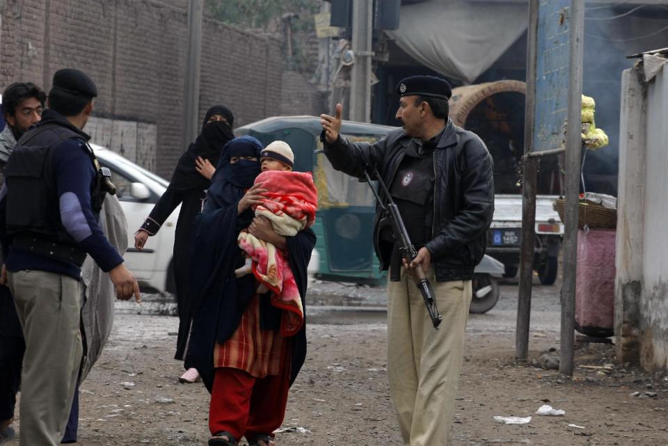 In this Feb. 2, 2014 photo, Pakistani police officer stand guard as people who need to vaccinate their children against polio approach health workers, in Peshawar, Pakistan. Pakistan's beleaguered battle to eradicate polio is threatening a global, multi-billion dollar campaign to wipe out the disease worldwide. Because of Pakistan, the virus is spreading to countries that were previously polio-free, U.N. officials say. (AP Photo/Mohammad Sajjad)