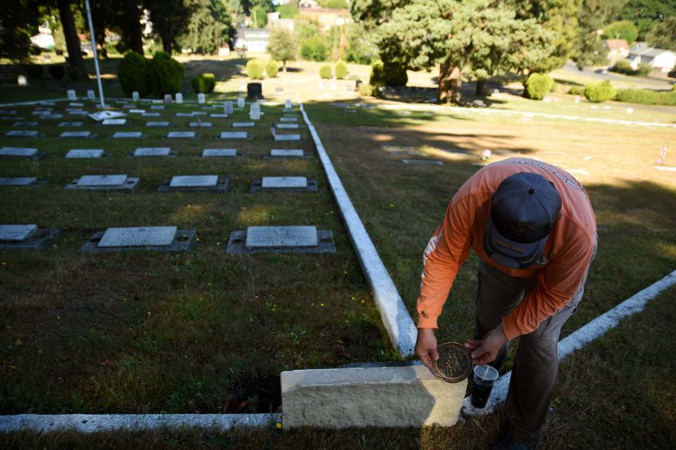 Mick Hersey bends down to demonstrate one of the six 12-inch-wide square flower boxes he plans to build at the corners of the veteran section at the Ivy Green Cemetery using sandstone blocks from the Harrison Hospital.