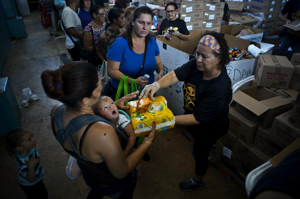 En esta fotografía del 7 de septiembre de 2018, una mujer con su hijo recibe pañales y gel de ducha gratis, mientras ella y otras personas hacen fila para recibir alimentos y otros artículos de primera necesidad donados por la organización sin fines de lucro Ministerio MARC, en Manati, Puerto Rico. Los trabajadores de beneficencia dicen que la mayoría de los necesitados que acuden a ellos son pensionistas enfermos, personas de la tercera edad, estudiantes y desempleados. (AP Foto/Ramón Espinosa)