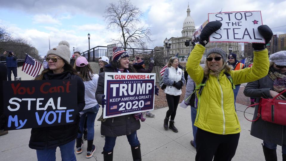 Protesters hold signs outside the Richard H. Austin state office building during a rally in Lansing, Mich., Saturday, Nov. 14, 2020. Michigan's elections board is meeting to certify the state's presidential election results. (AP Photo/Paul Sancya)